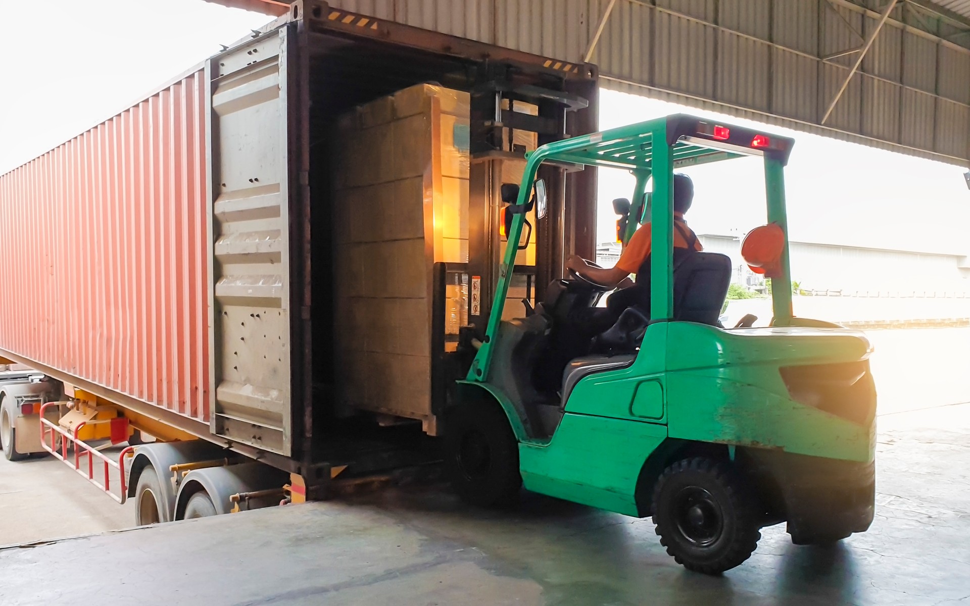 Forklift driver loading goods pallet into the truck container, freight industry warehouse logistics and transport